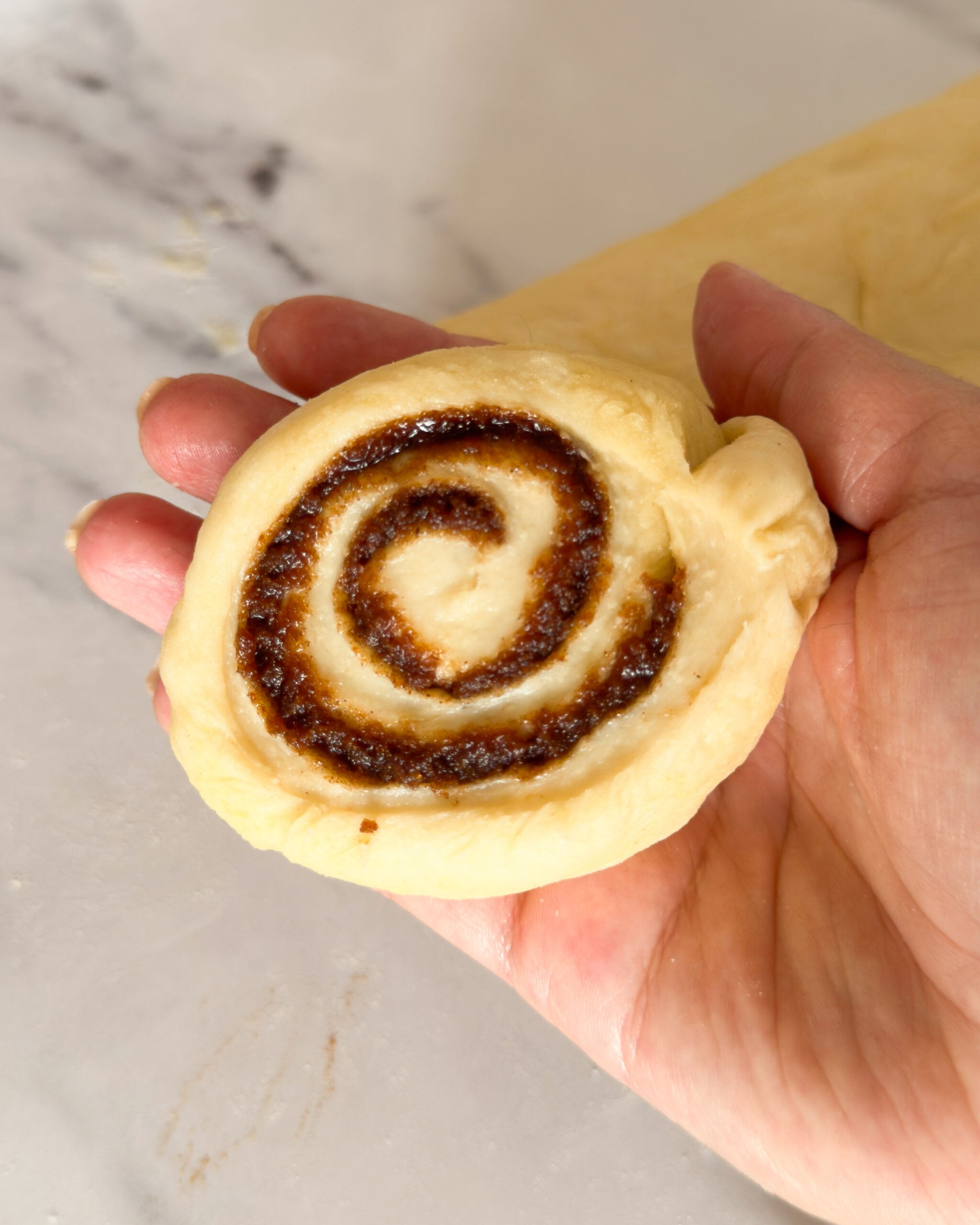 cut cinnamon roll in hand, before baking