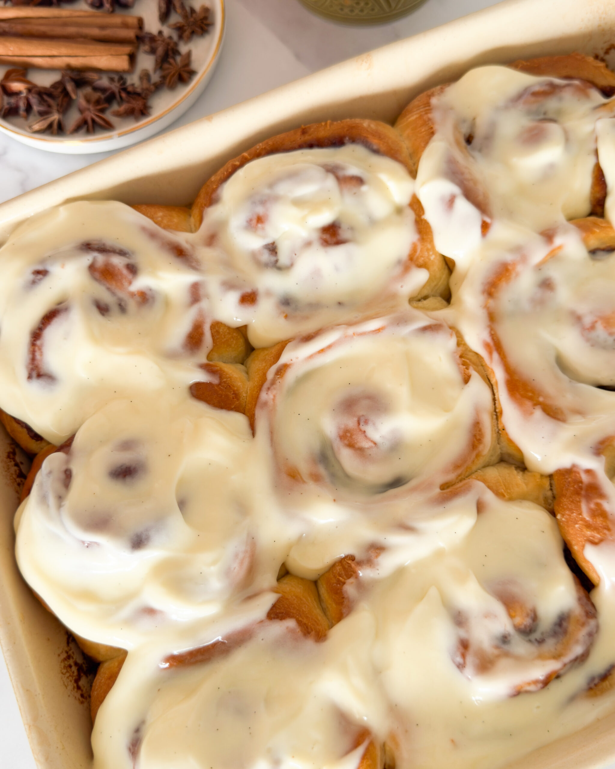 Baked cinnamon rolls in baking dish, topped with cream cheese icing